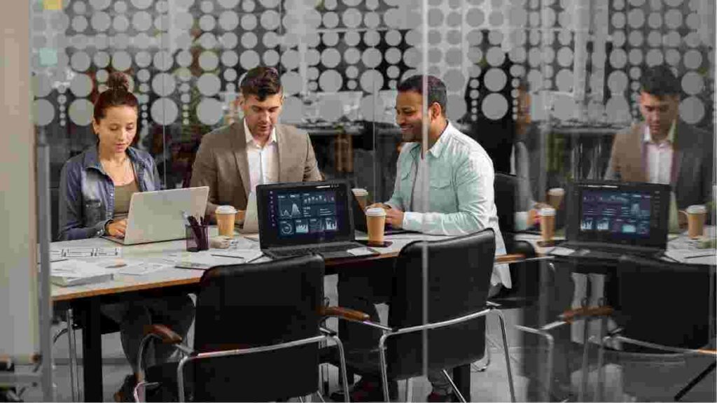 Professionals collaborating in a modern office with laptops and data screens.