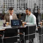 Professionals collaborating in a modern office with laptops and data screens.